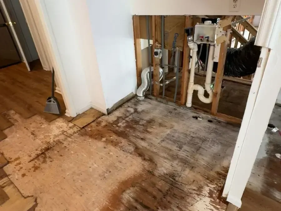 A wall cut open around the plumbing with the soaked flooring lifted