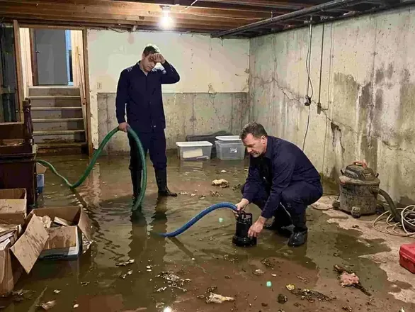 Two techs pumping standing water out of an unfinished basement