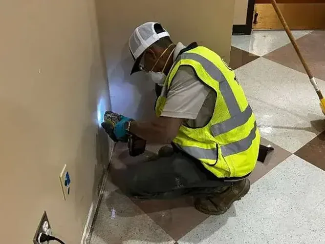 A technician in a safety vest pressing a moisture meter against a damp wall