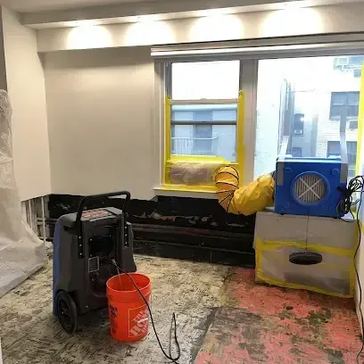 Restoration equipment, including air movers and a dehumidifier, drying a room damaged by water inside a home