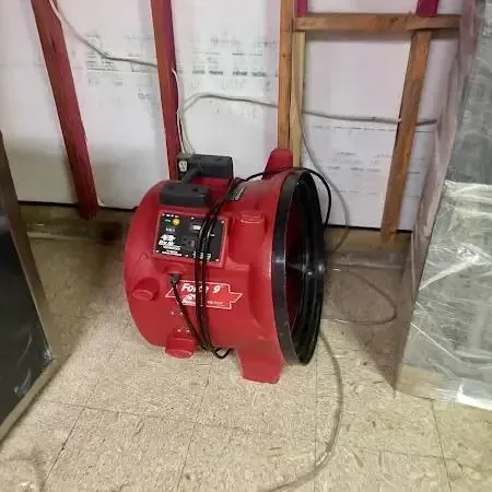 A red air mover running in a room with an opened lower wall and hanging plastic sheeting