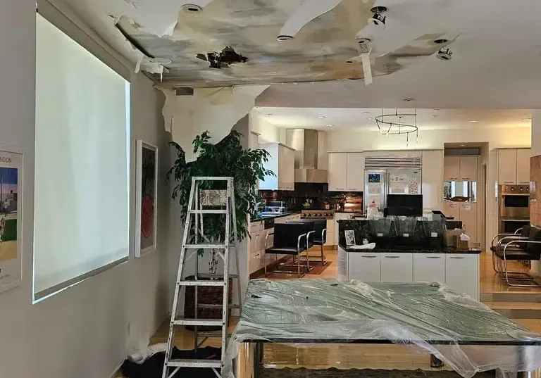 An opened ceiling and plastic sheeting in a room where rain leaked through the roof