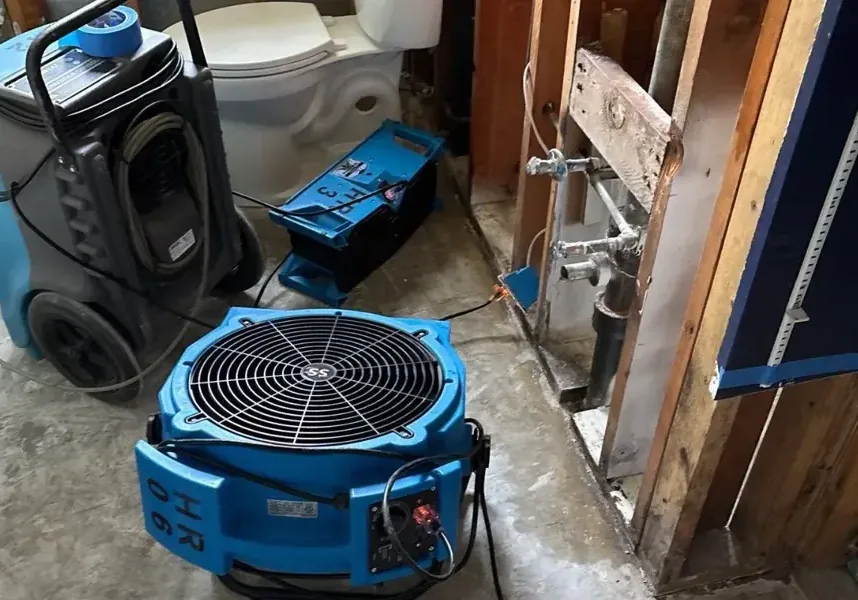 An air mover and a dehumidifier drying an opened wall down to the framing
